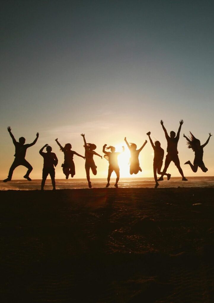Silhouette of a group of friends jumping on a beach at sunset, expressing joy and freedom.